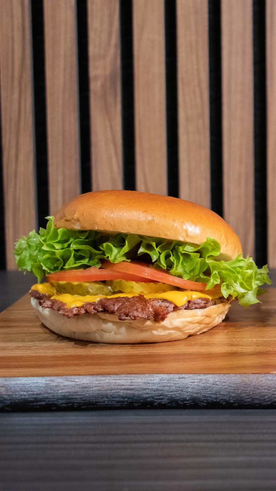 A cheeseburger on a wooden board in front of a slatted wood wall
