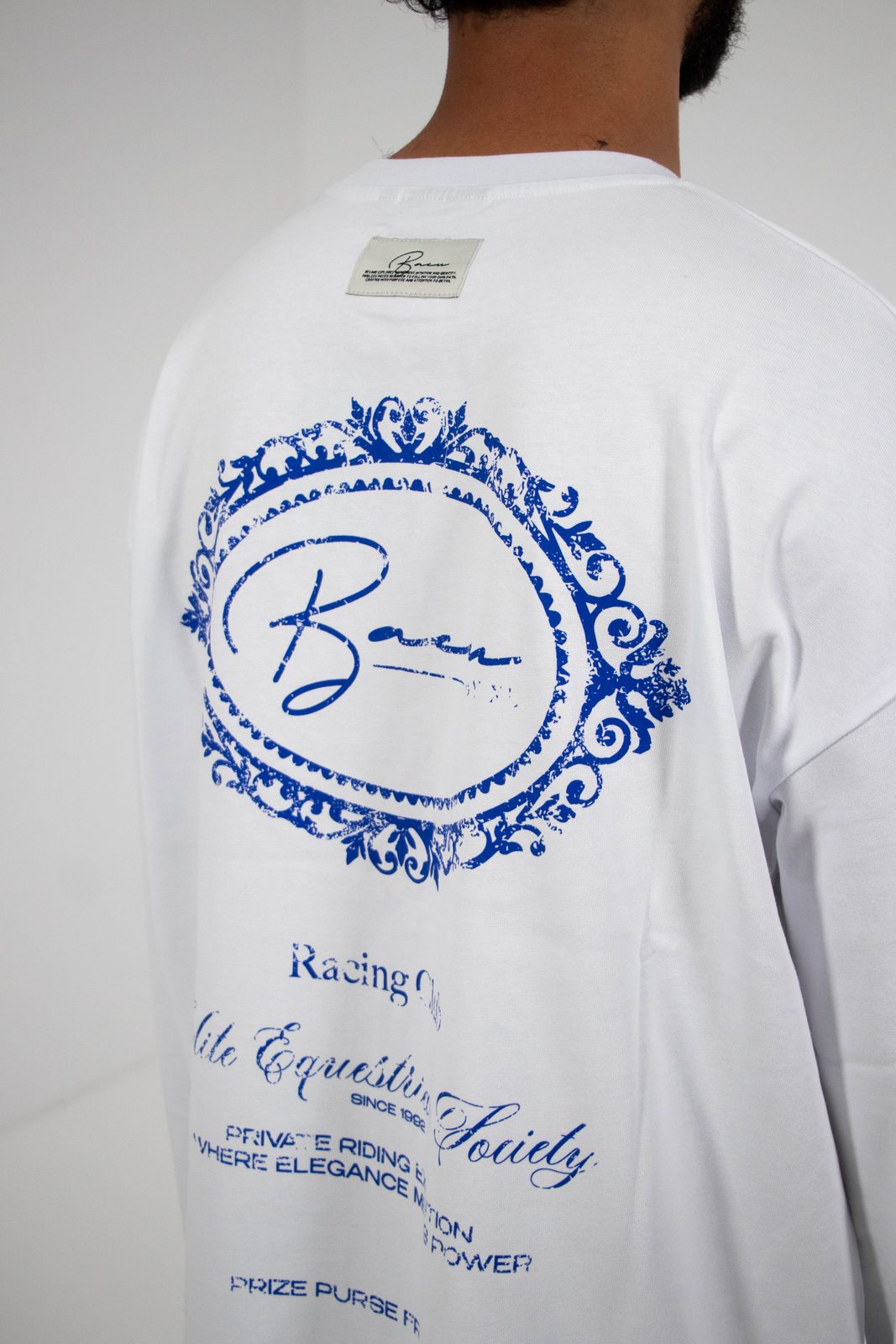 Back of a white BACU longsleeve with an ornate blue oval print