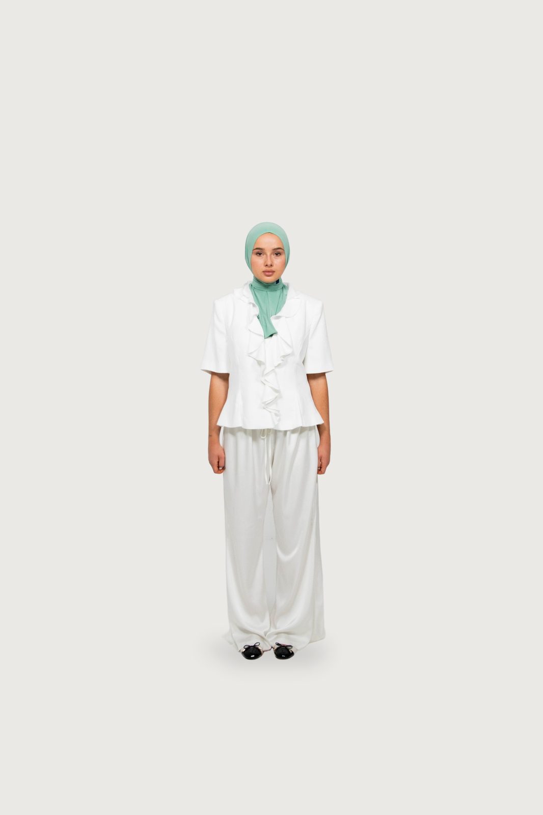 Model in a green hijab, white ruffled blouse and wide trousers