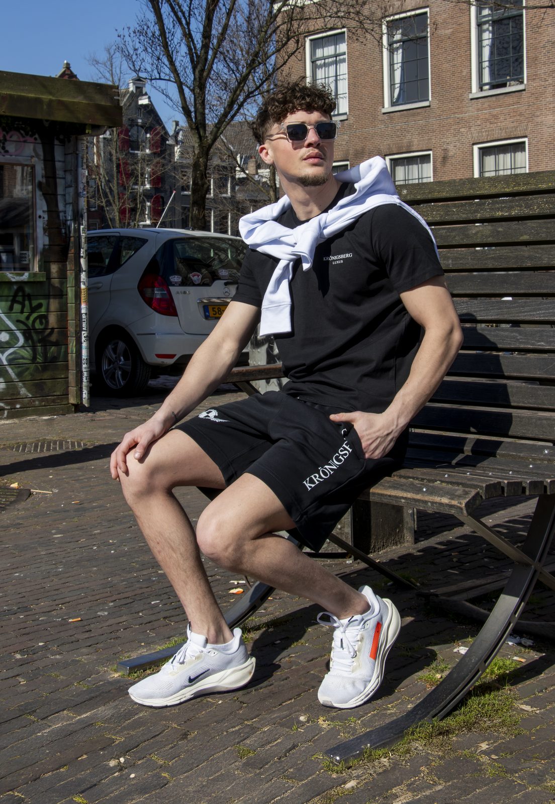 Model on a bench in a black Kronigsberg tee and shorts