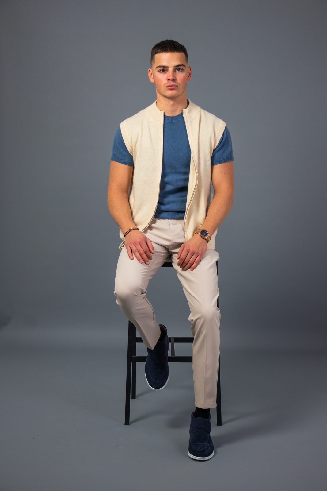 Model on a stool in a cream knitted NOBA vest over a blue tee