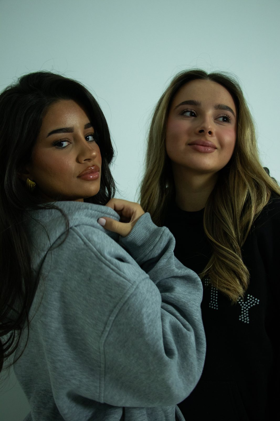 Two models in Varsity hoodies on a pale blue backdrop
