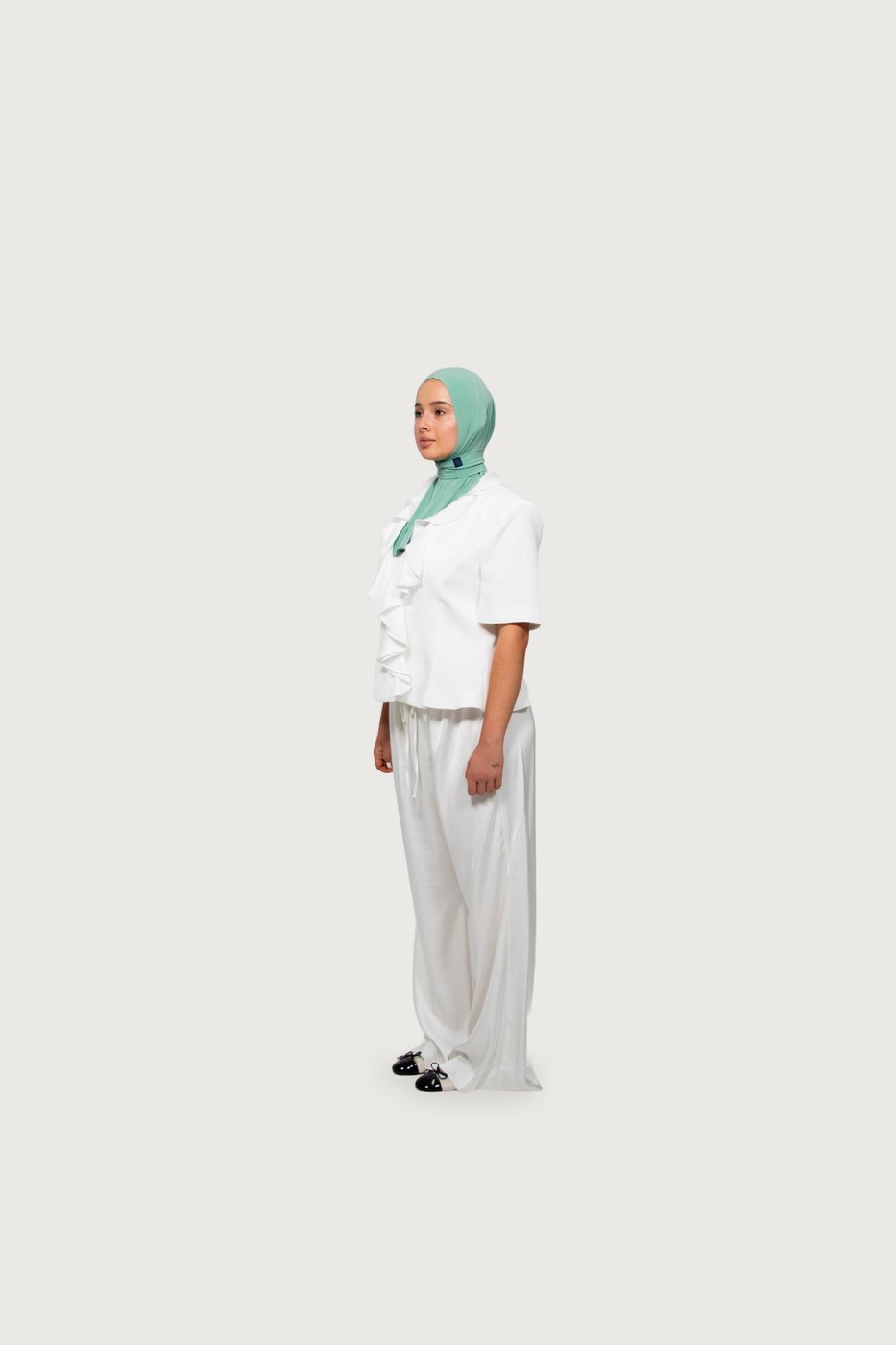 Model in a white ruffled blouse and wide trousers with a mint hijab