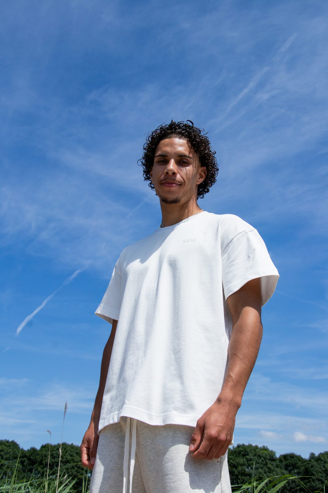 Model in a white LMF tee and shorts shot from below against a blue summer sky