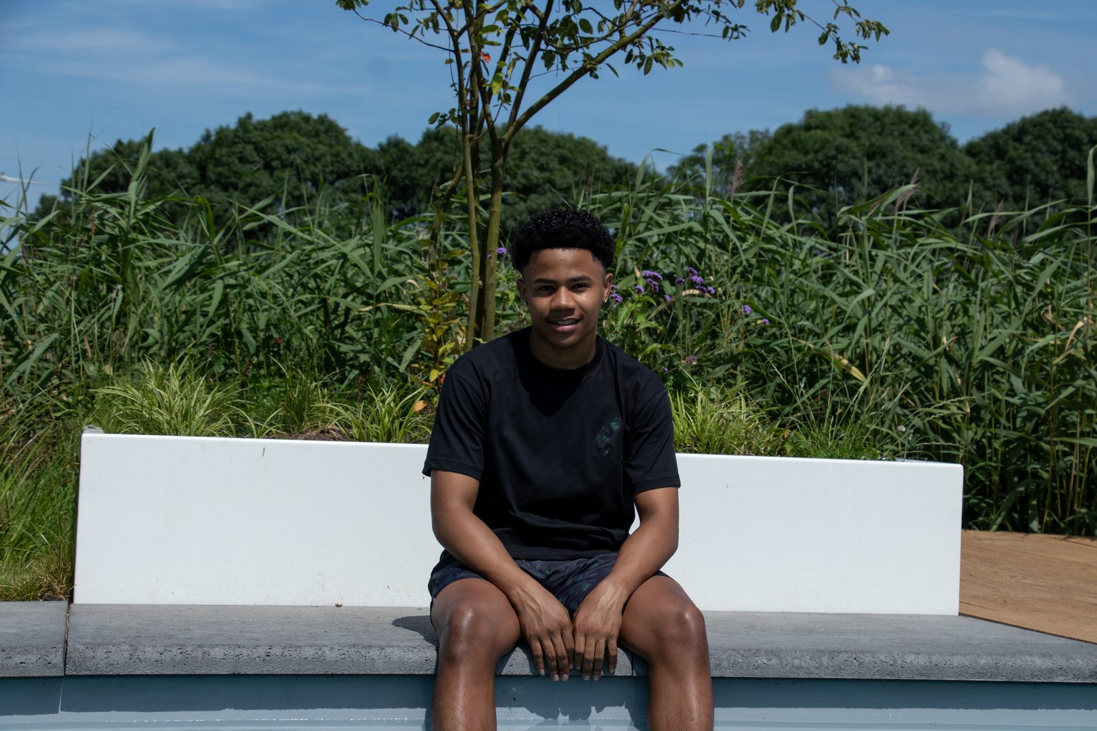 Model sitting on the pool edge in a black LMF tee