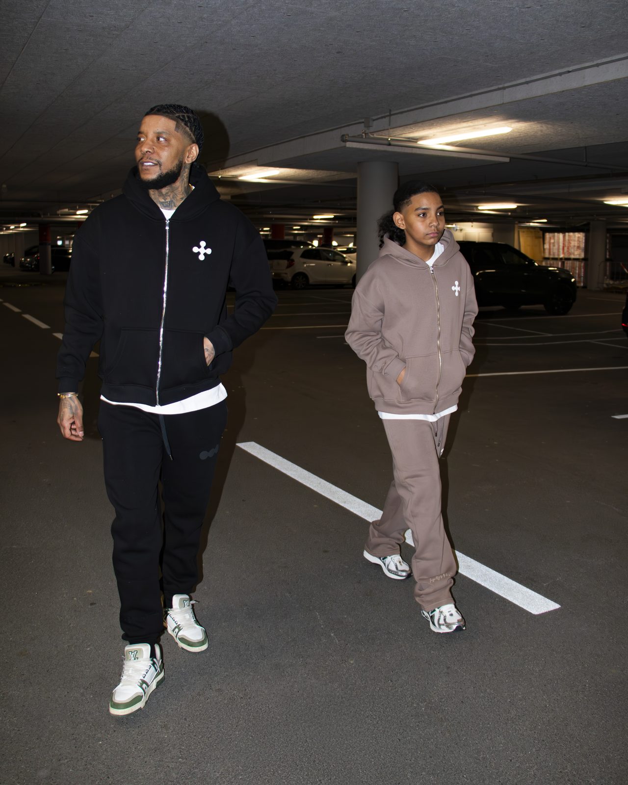 Two models in black and taupe LMF tracksuits walking through a parking garage