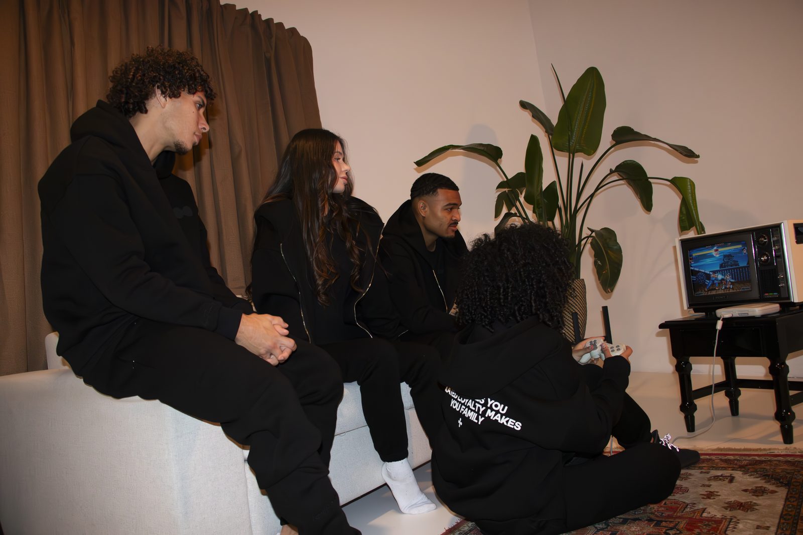 Friends in black LMF tracksuits on a white sofa