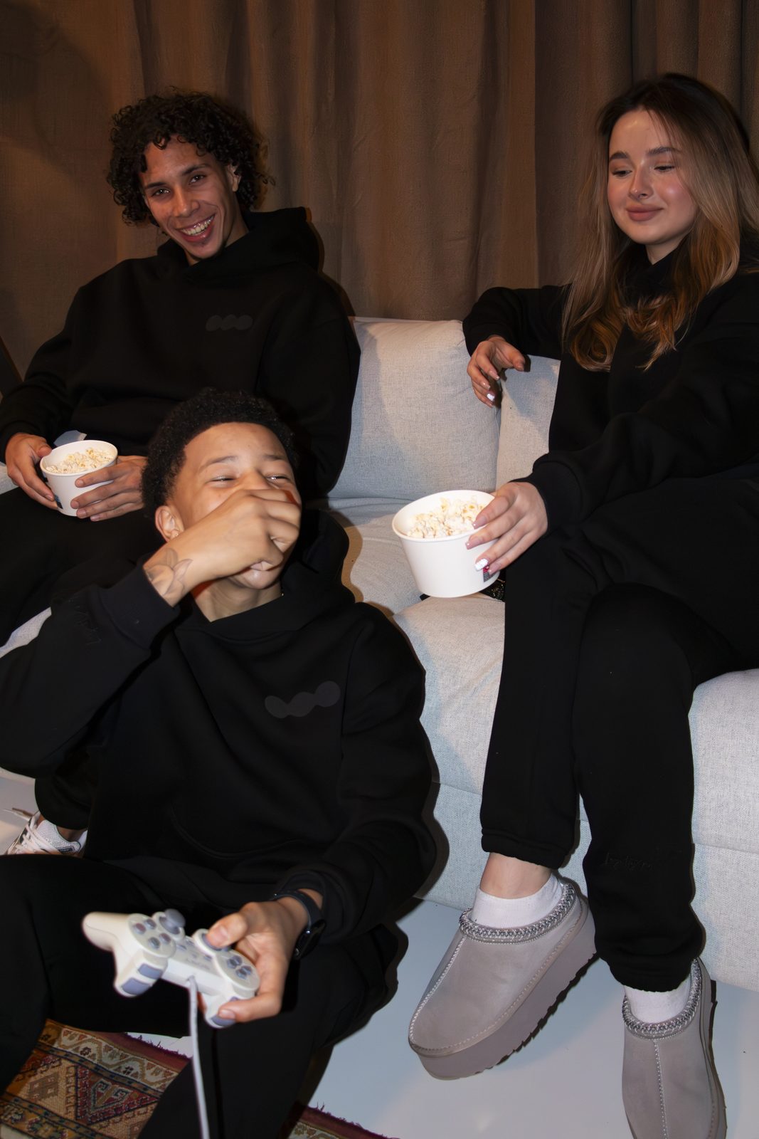 Friends laughing on a sofa in black LMF tracksuits