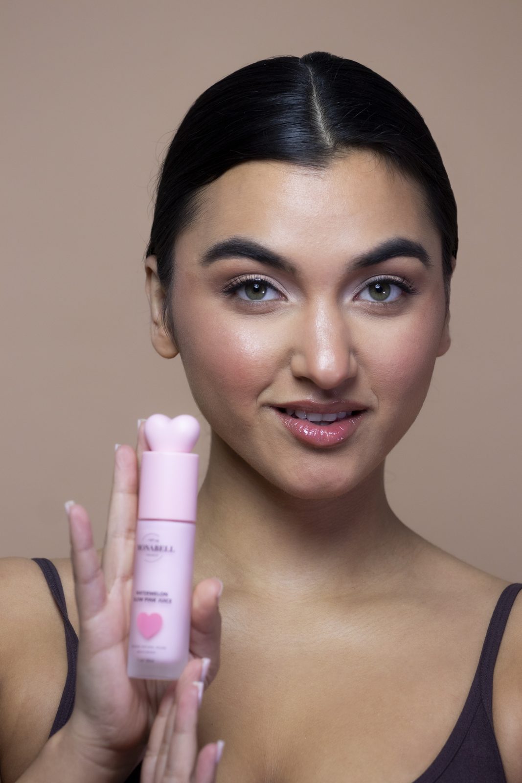 Model holding a pink Monabell Watermelon Glow bottle beside her face