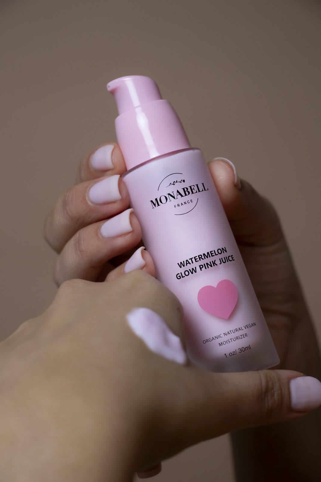 Hands holding a pink Monabell Watermelon Glow bottle with a drop of serum