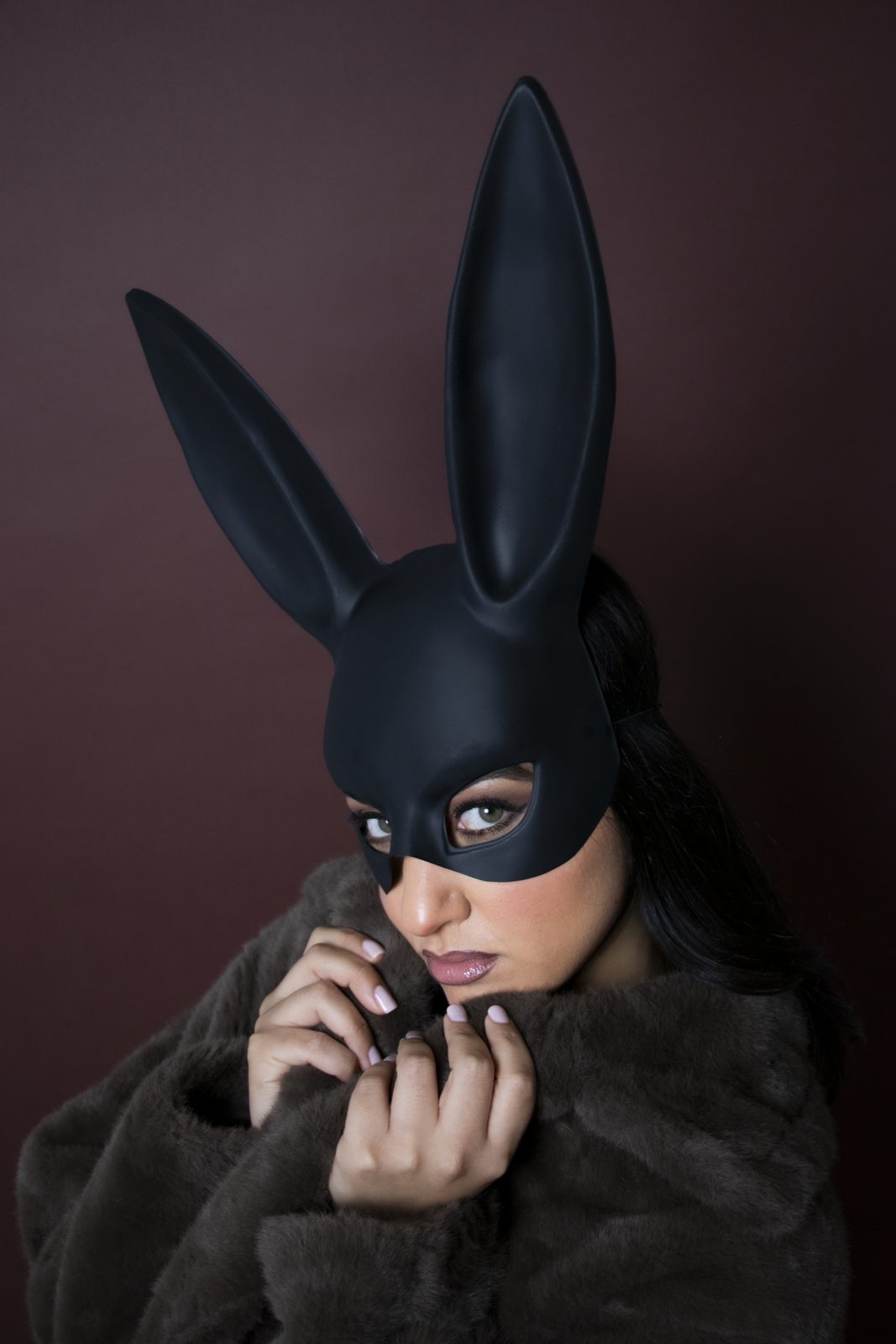 Model in a bunny mask pulling a dark fur coat around her