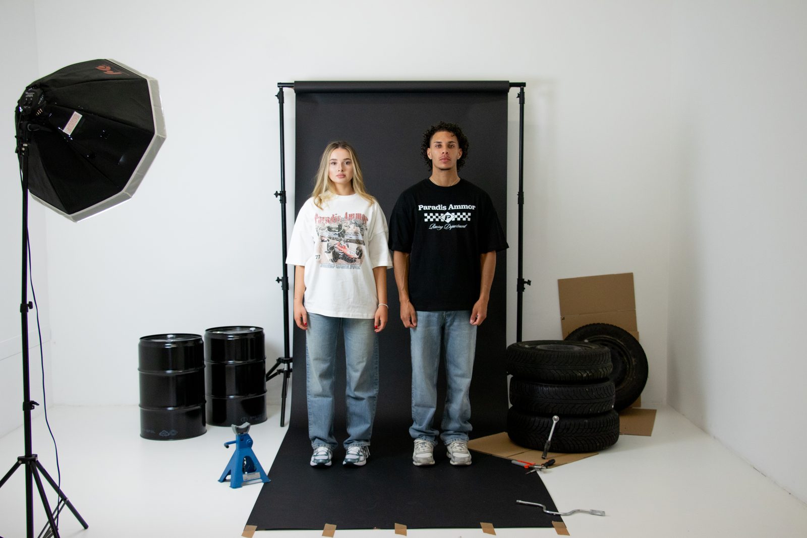 Wide view of the racing set: a softbox, black backdrop, stacked tyres, barrels and a jack
