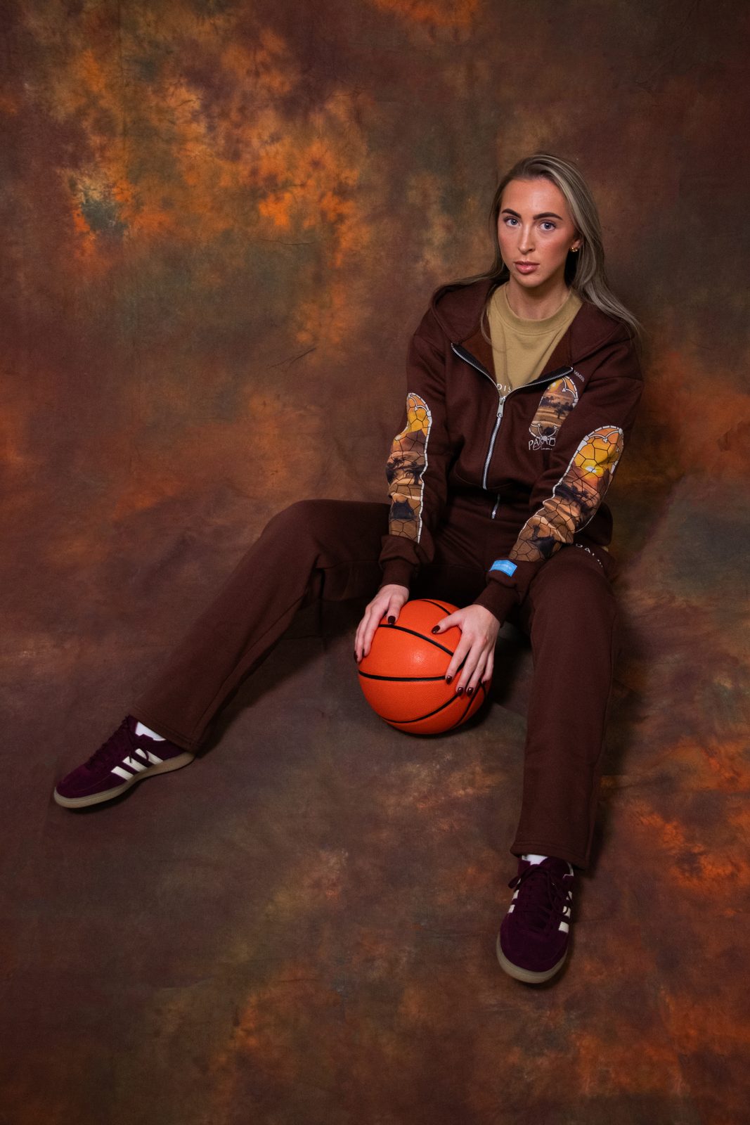 Model sitting on the floor with a basketball in a brown Paradis tracksuit