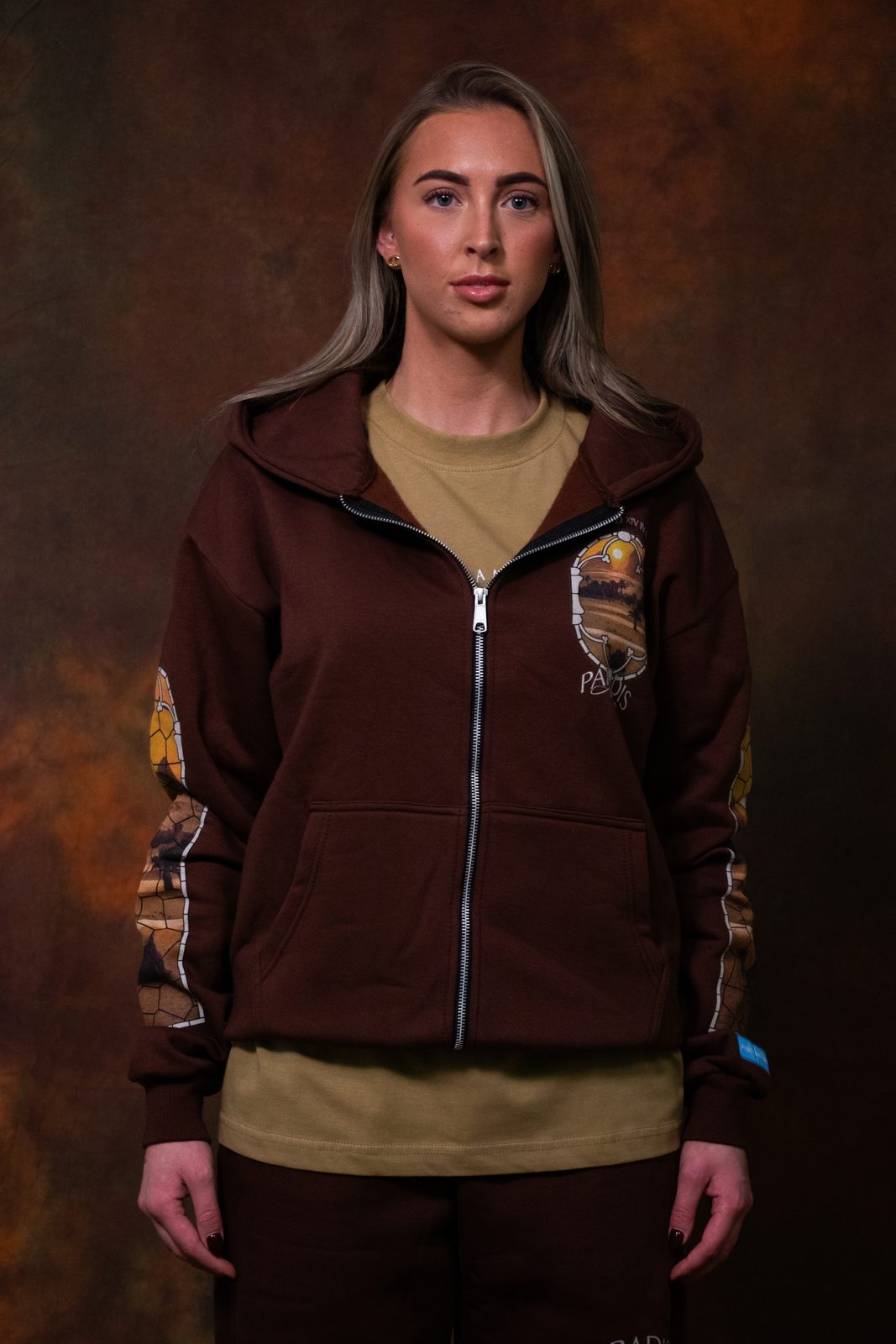 Model in a brown Paradis zip hoodie over a tan tee