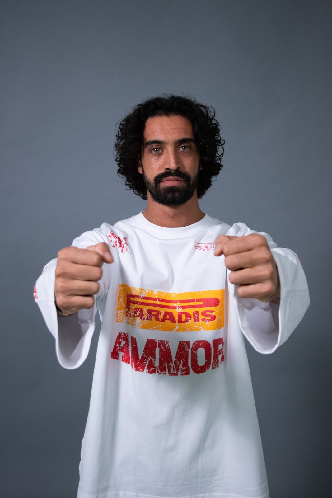 Model holding out a white Paradis Ammor racing longsleeve against a grey backdrop