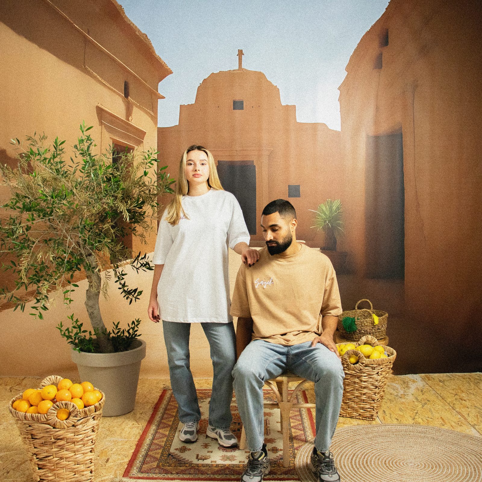 Model in a white tee standing behind a seated model in a sand tee on the Marrakech set