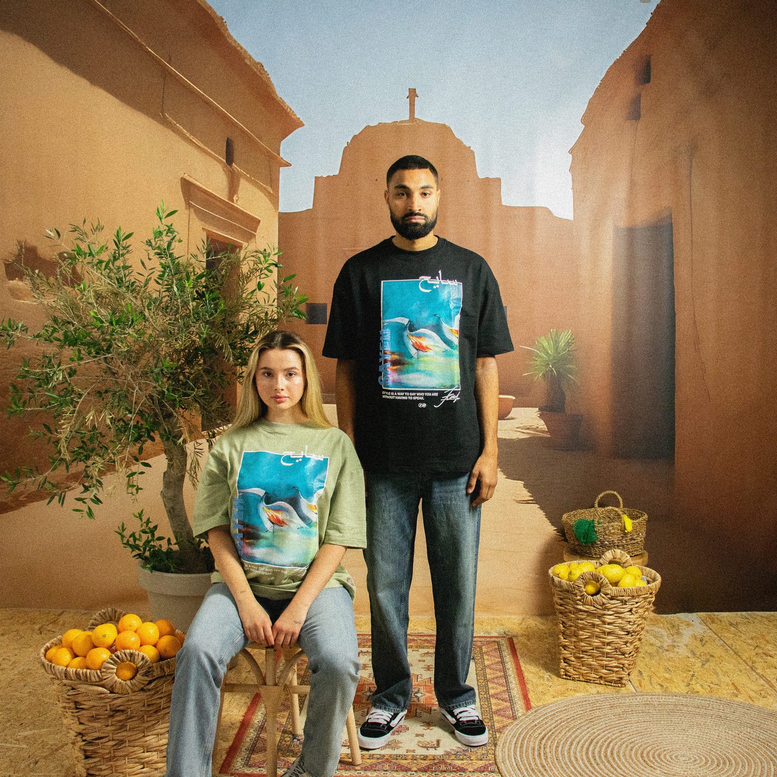 Model in a green tee seated in front of a model in a black SAYEH tee