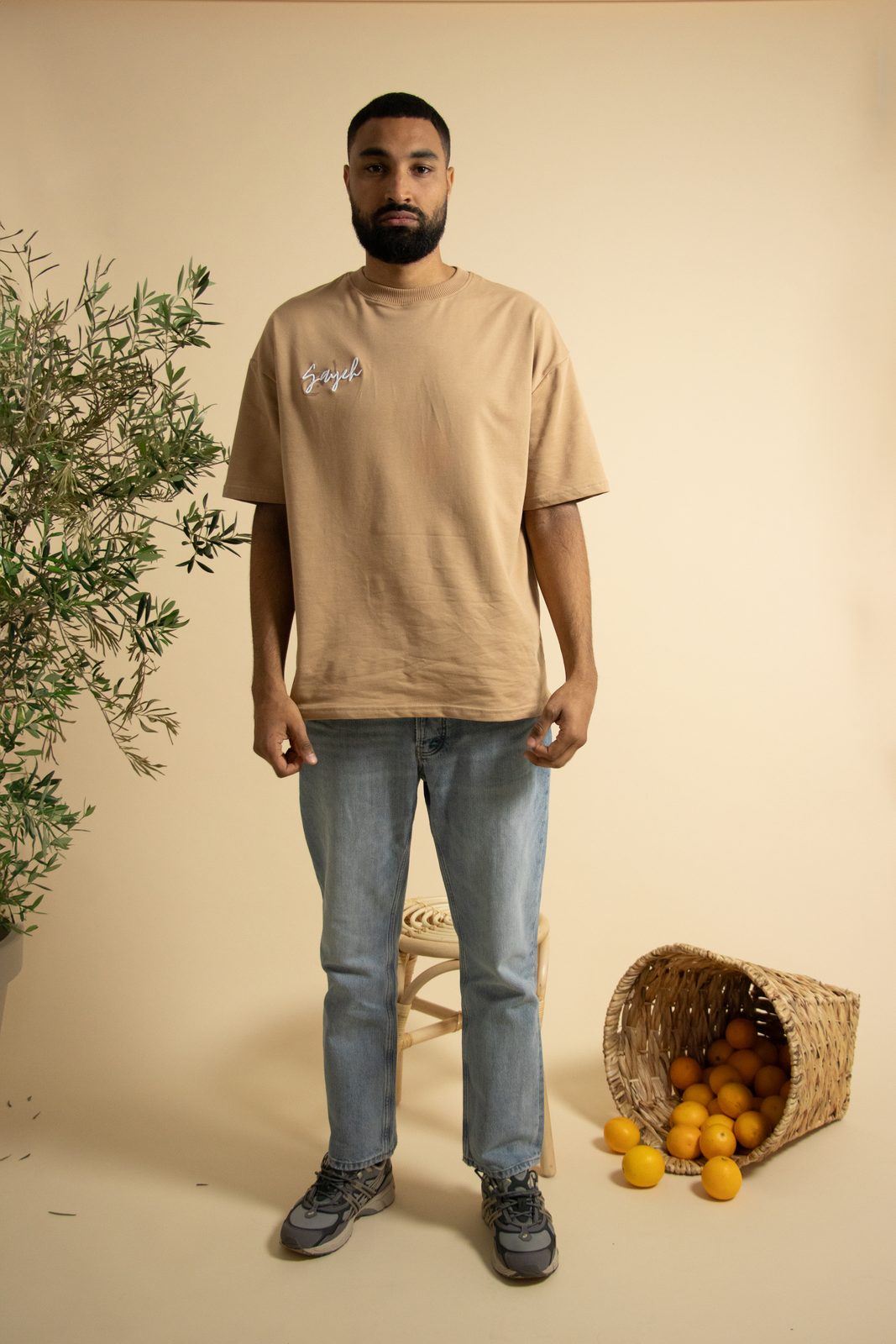 Model in a sand-coloured SAYEH tee next to an olive branch