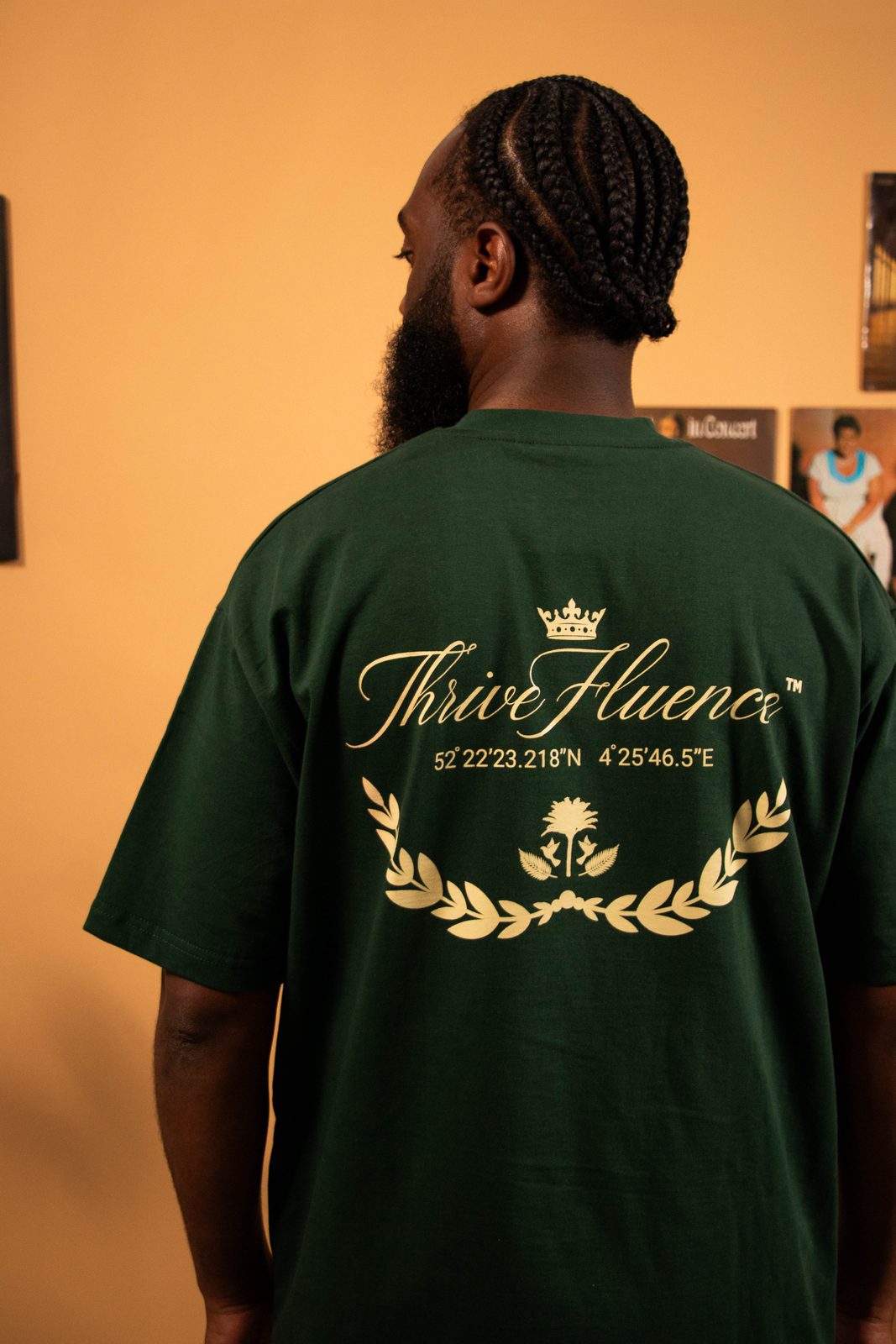 Back of a green Thrivefluence tee with a gold crest print