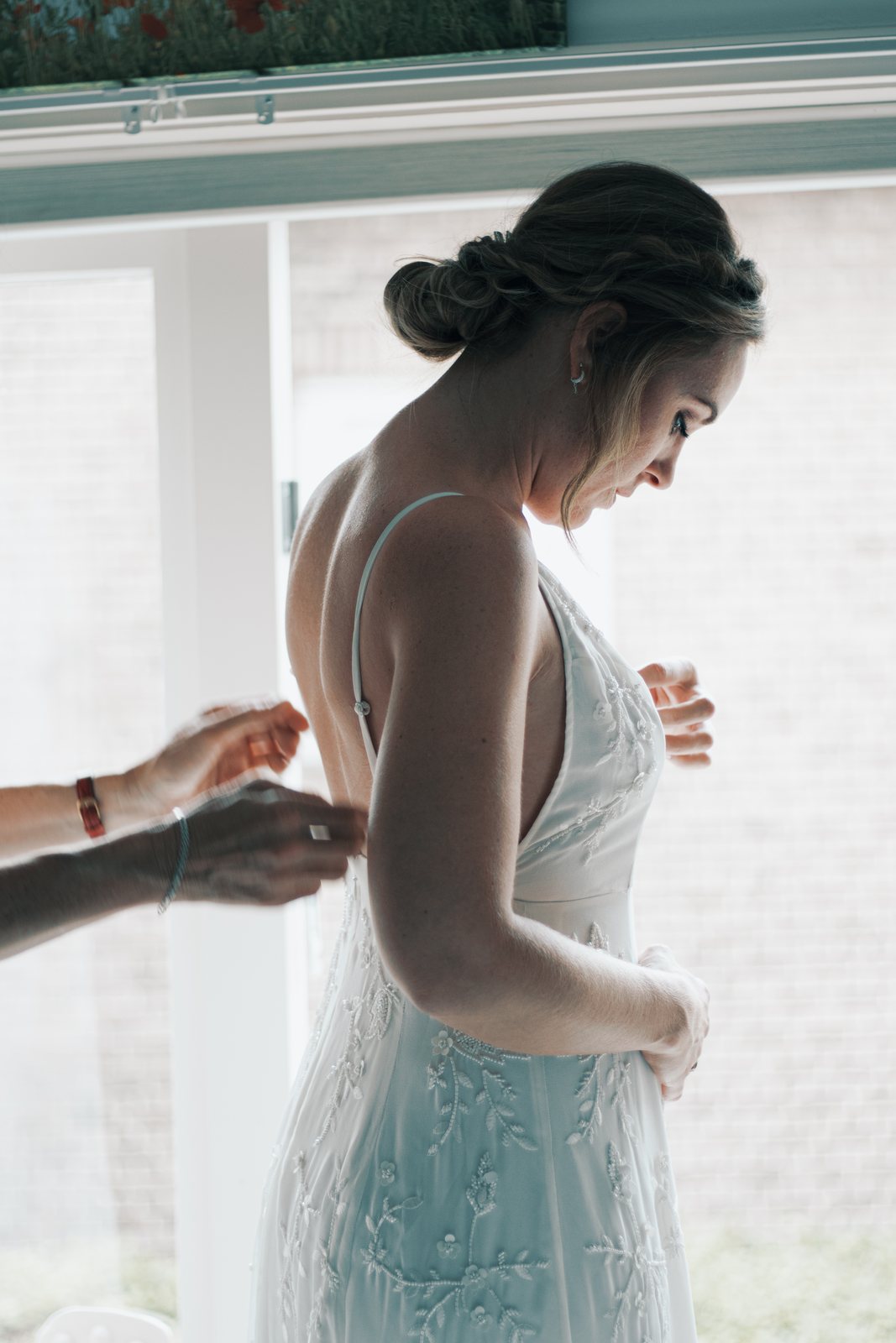 Imre being buttoned into her wedding dress by a bright window