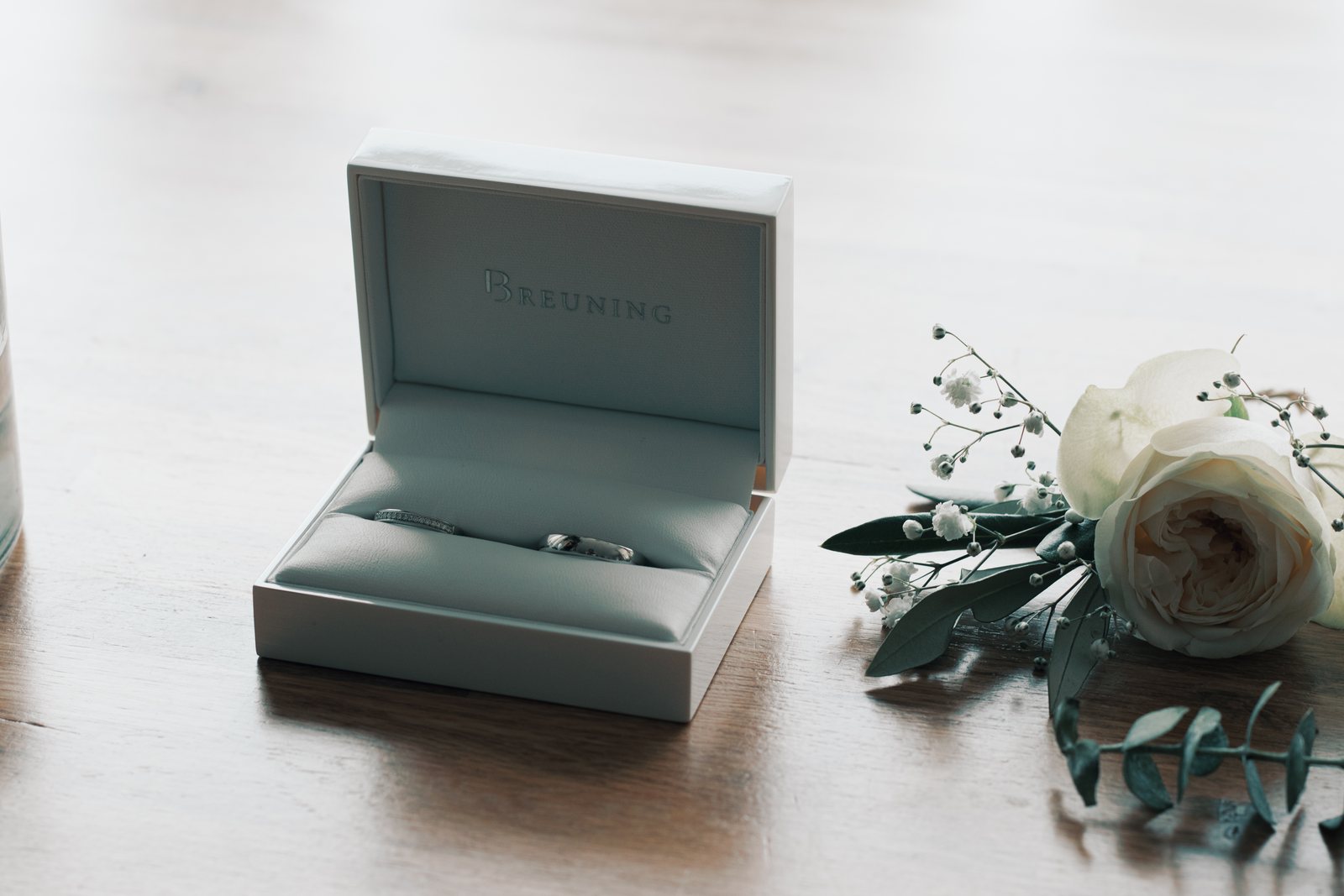 The wedding rings in an open box beside a white rose boutonniere