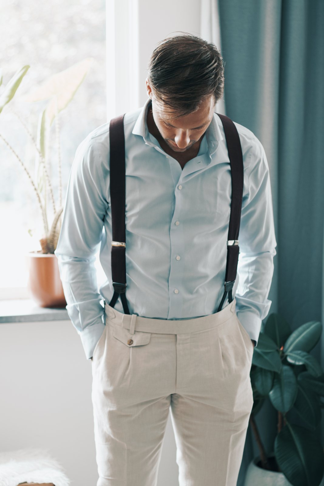 Chris in a light blue shirt and braces looking down, hands in his pockets