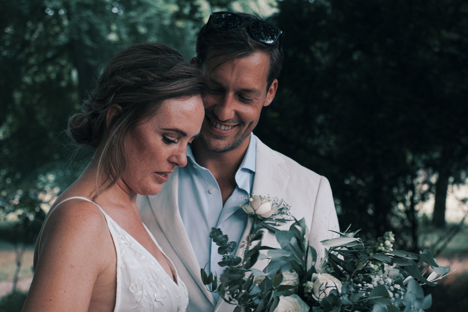 Imre leaning into Chris with her eyes lowered, holding her bouquet