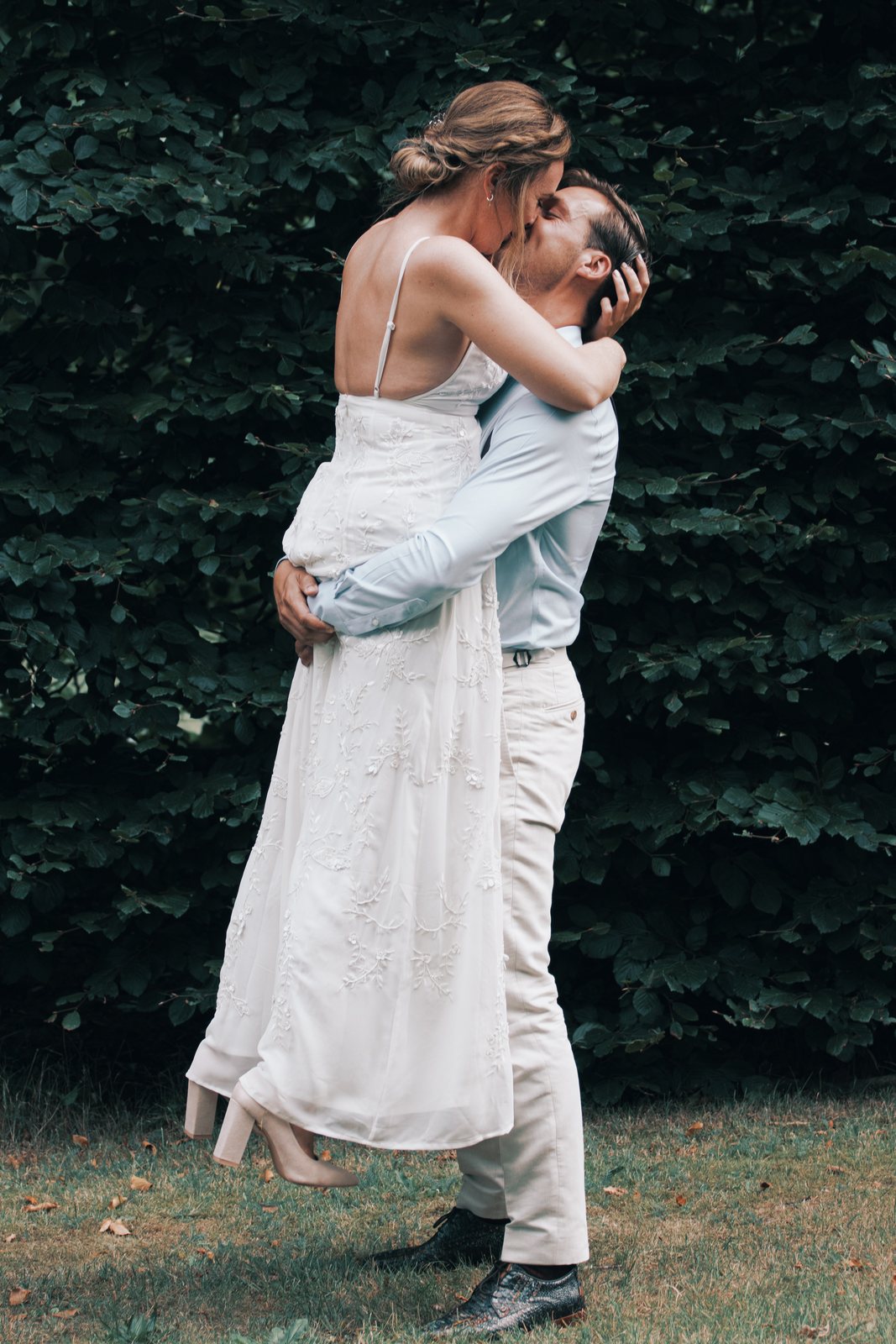 Chris lifting Imre off the ground for a kiss against a dark hedge