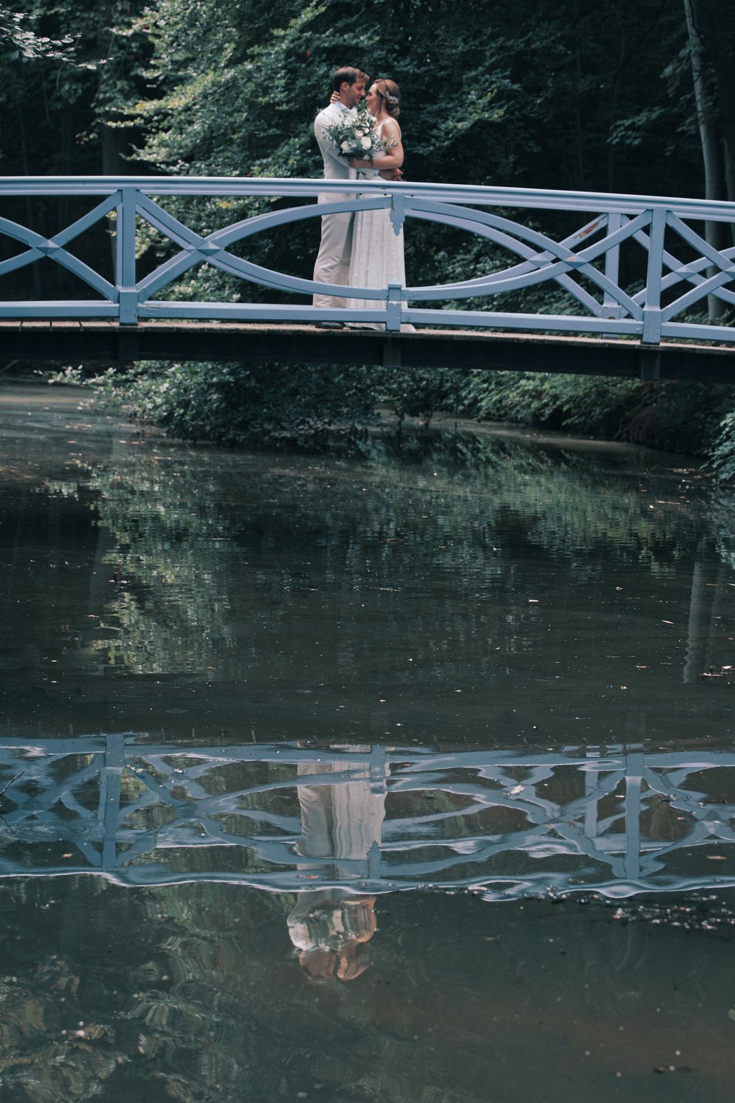 Imre and Chris kissing on a blue wooden bridge, reflected in the water below