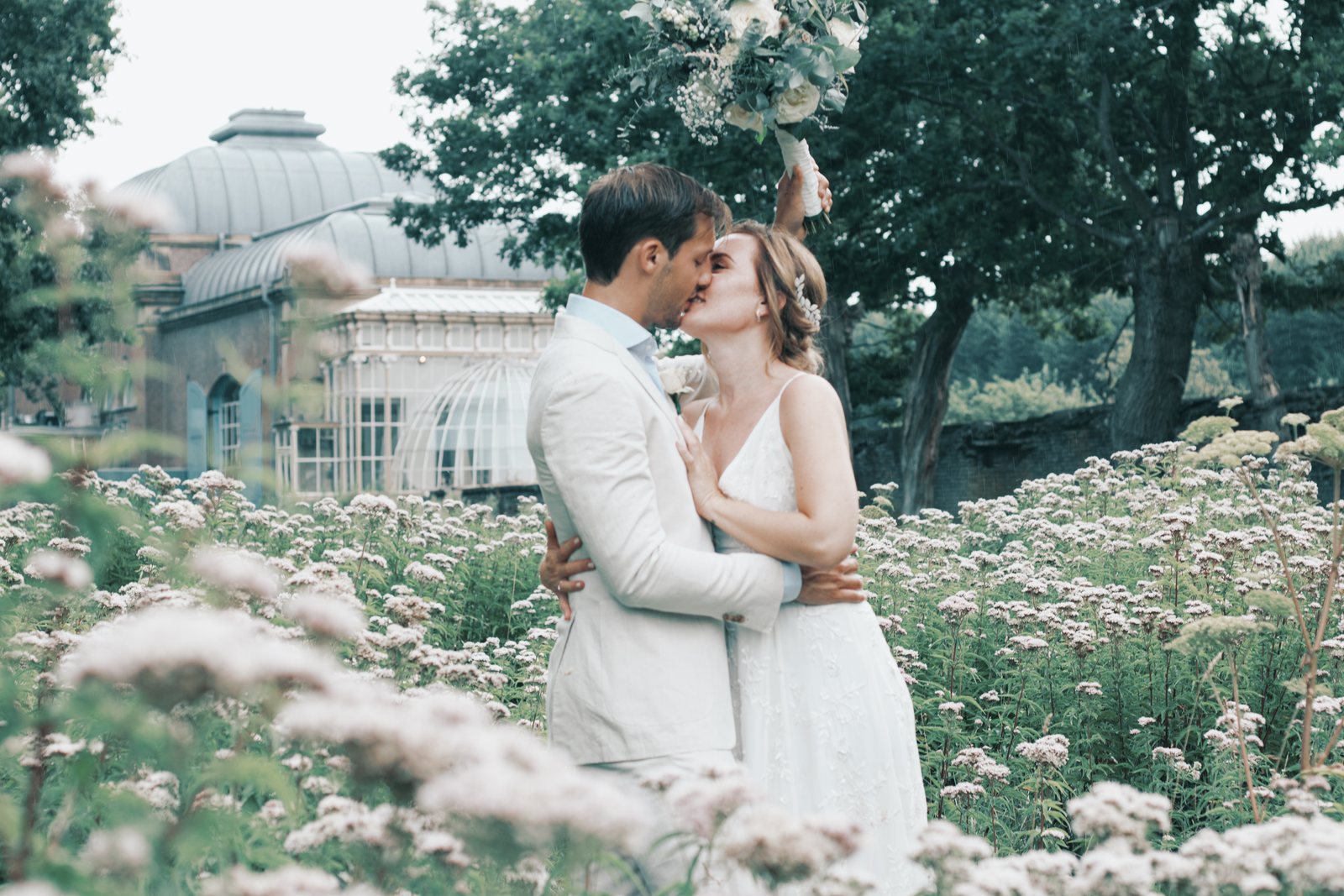 Imre and Chris kissing among wildflowers in front of a glass palm house