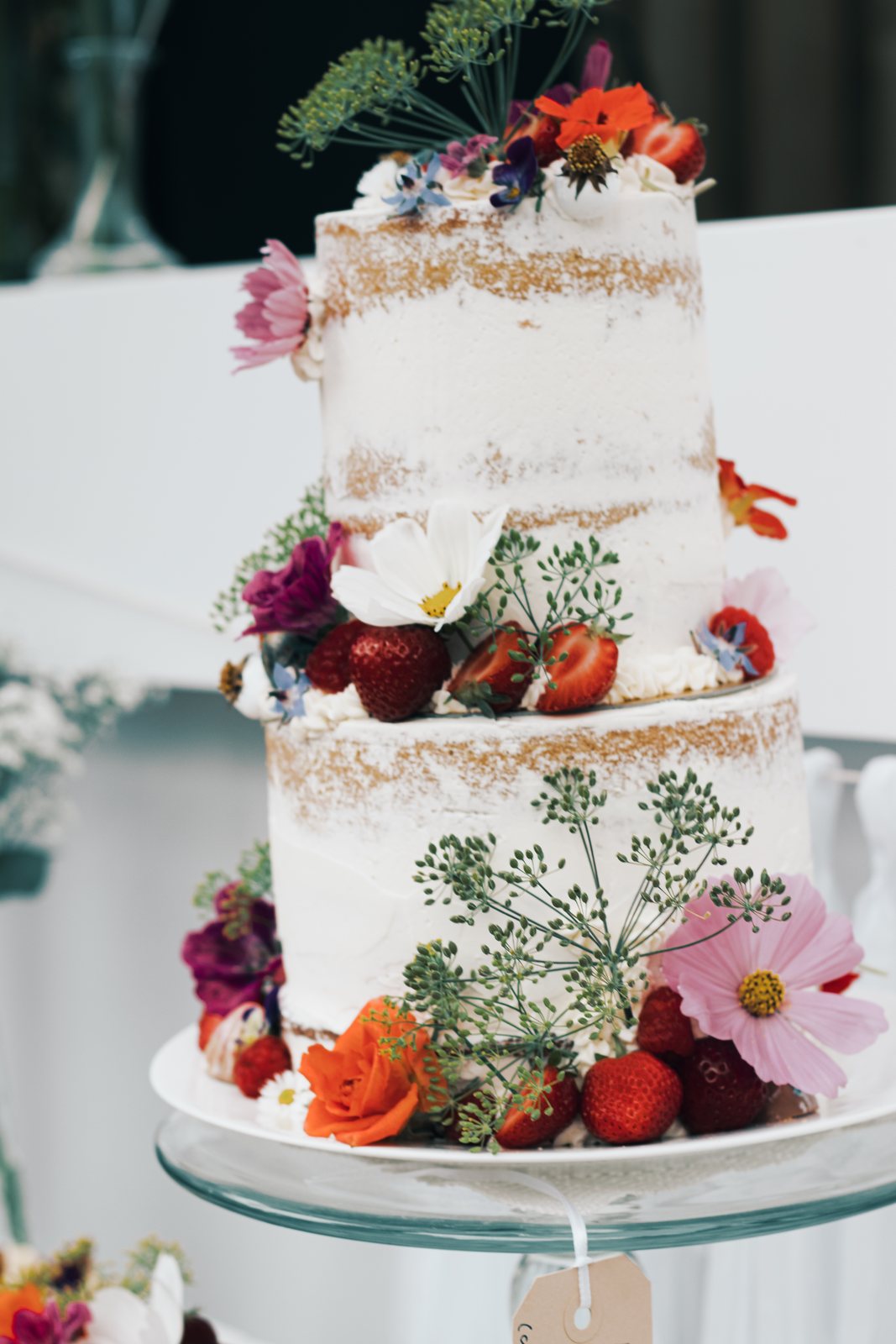 A naked wedding cake decorated with strawberries and fresh flowers