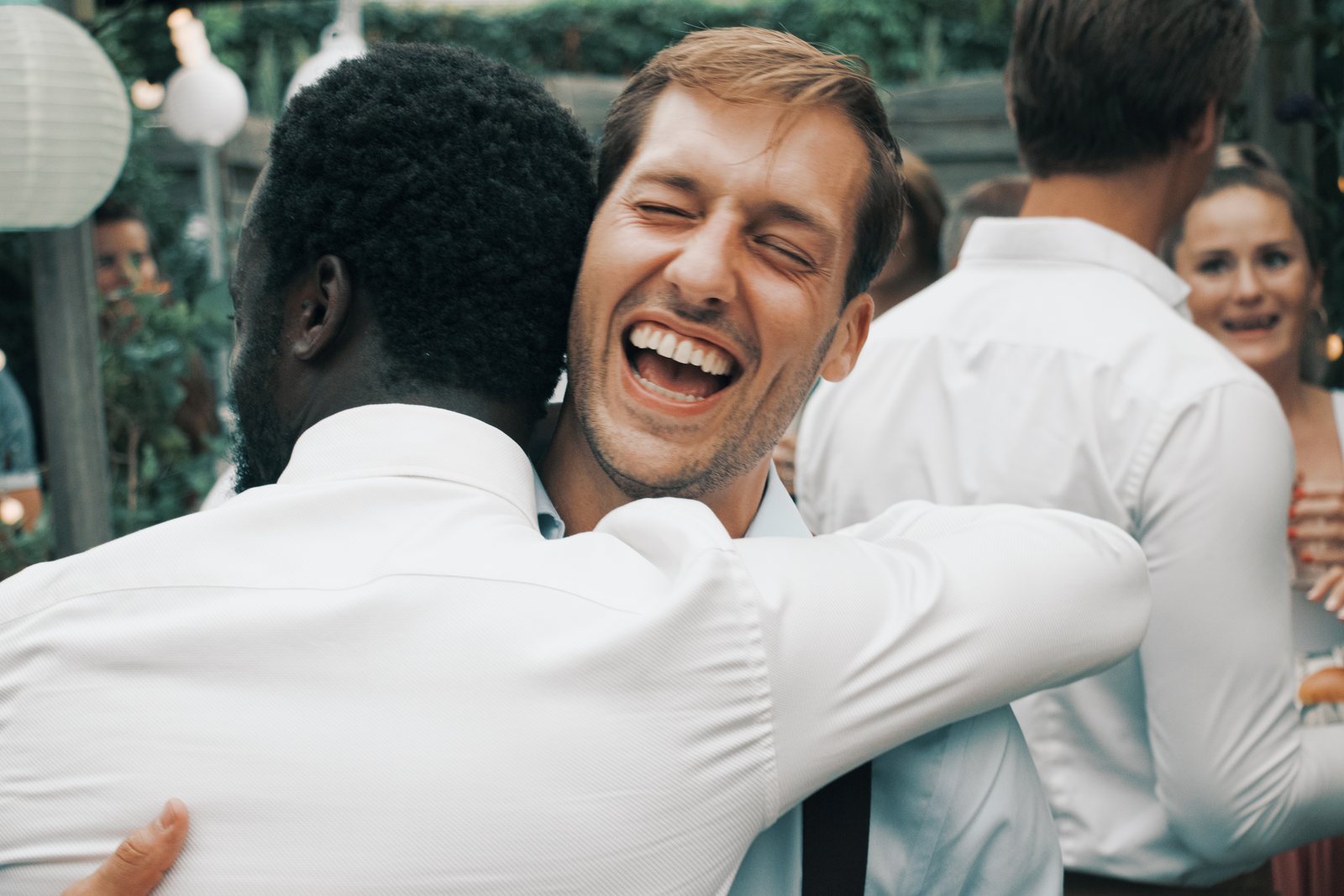 Chris laughing with his eyes shut while hugging a friend