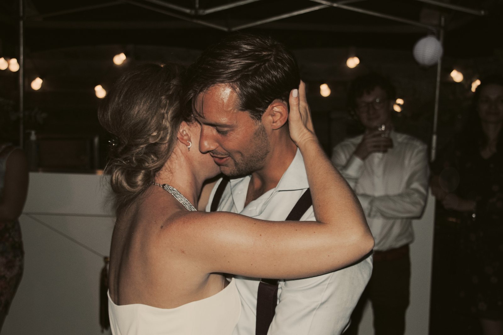 Imre and Chris kissing on the dance floor under festoon lights
